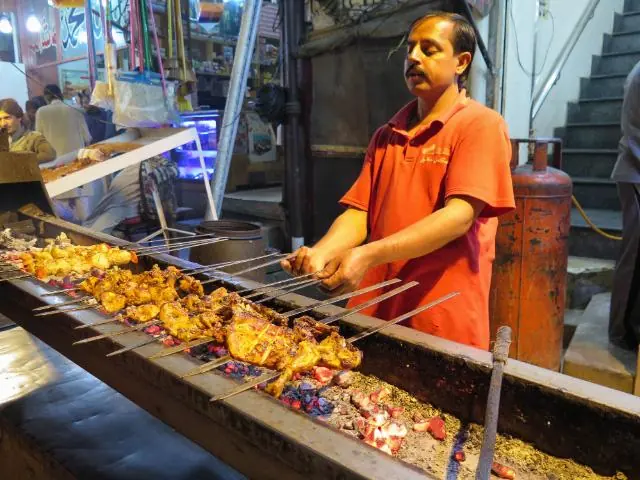 A cook grilling chicken tikka skewers at a Lahore food stall