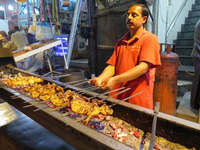 A cook grilling chicken tikka skewers at a Lahore food stall