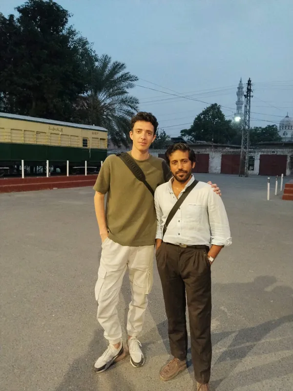 A travel YouTuber and his Past Enlighten guide at a railway heritage site in Lahore, with a mosque minaret behind